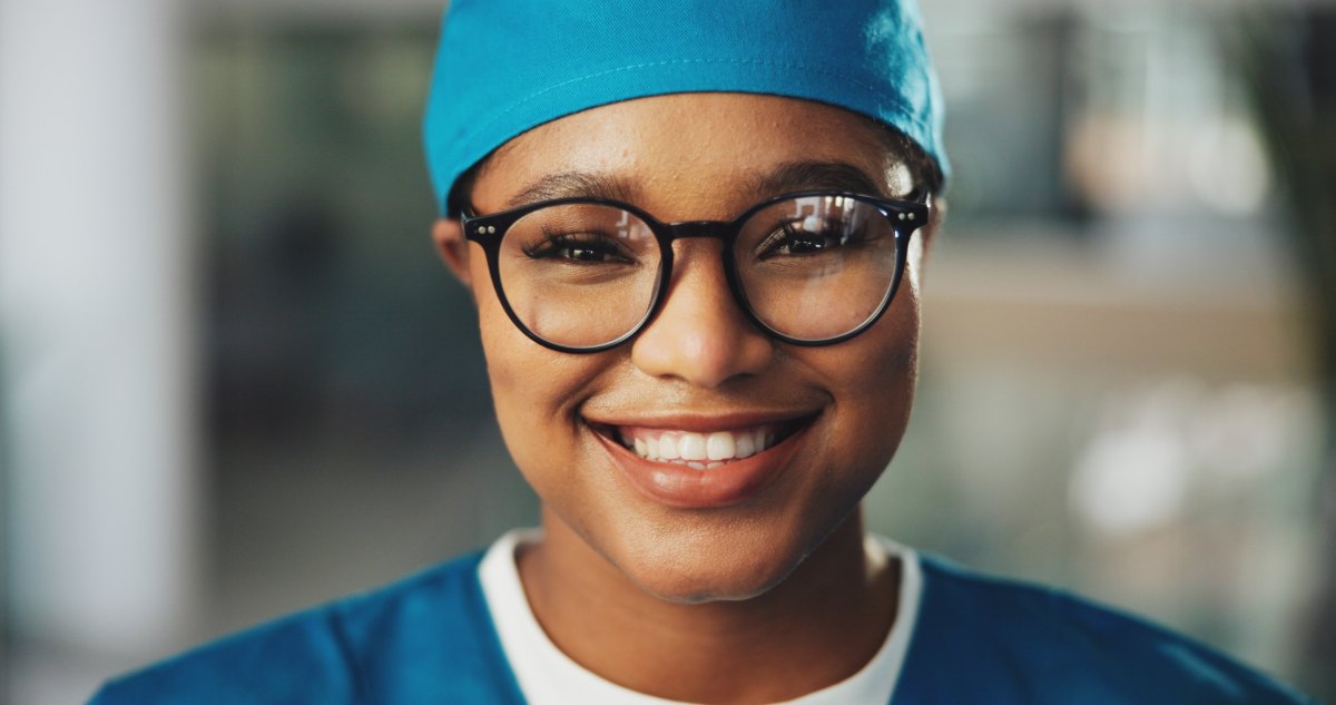 A theatre clinician in scrubs and surgical cap, smiling